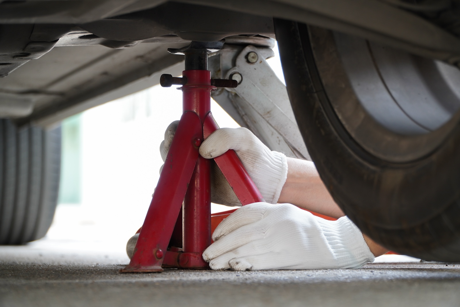 Mechanic wearing white gloves placing a red jack stand underneath a vehicle