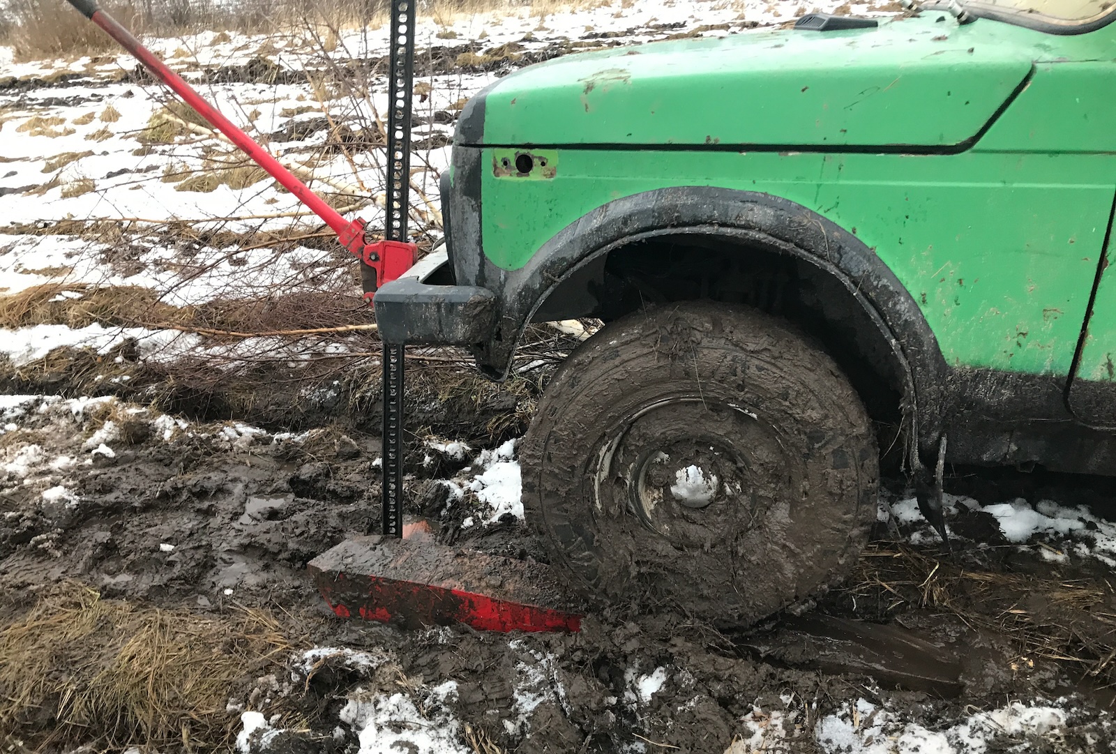 Green truck stuck in mud raised with a hi-lift