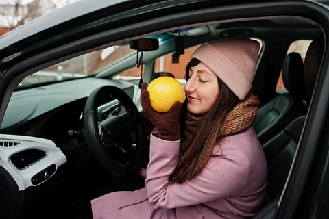 A woman sitting in a car, sniffing a lemon.